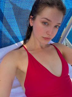 a woman in a red top sitting on a beach chair with her arm around the back of an umbrella