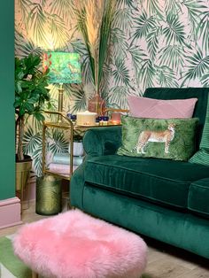 a living room filled with green furniture and walls covered in tropical wallpaper, including a pink ottoman