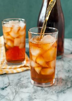 a pitcher pouring ice into a glass filled with iced tea on top of a marble table