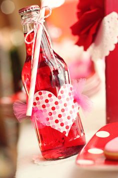 a bottle filled with red liquid sitting on top of a table next to a heart shaped cookie