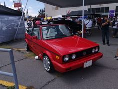 a red car parked in front of a building with people standing around and looking at it