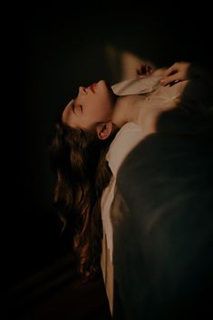 a woman laying down in the dark with her eyes closed