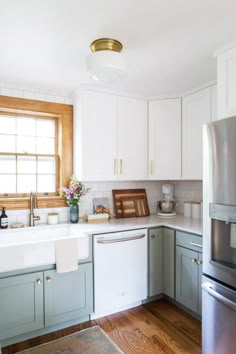 a kitchen with white cabinets and light green painted cupboards, wood flooring and stainless steel appliances