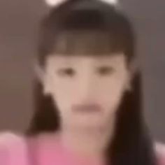 a blurry photo of a woman with long black hair wearing a pink shirt and looking at the camera