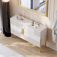 a white vanity with gold accents in a bathroom next to a mirror and towel rack