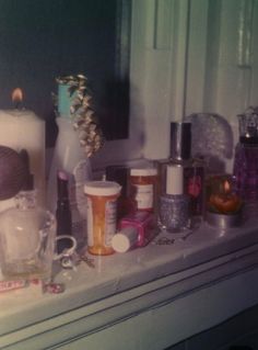 various items are sitting on a shelf in front of a window with candles and bottles