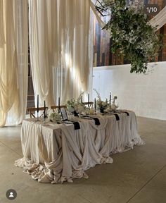 the table is covered with white cloths and decorated with greenery, flowers and candles