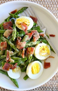 a white plate topped with asparagus and hard boiled eggs next to a fork