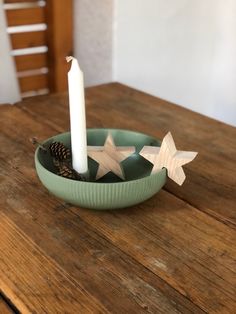 a candle is sitting in a bowl on a table with two stars and a pine cone