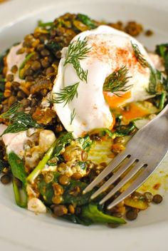 a white plate topped with an egg and vegetables next to a fork on top of a table