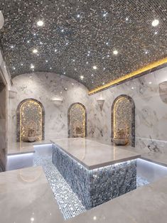 an indoor swimming pool surrounded by white marble and blue glass mosaic tiles with lights on the ceiling