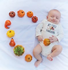 a baby in a white bodysuit surrounded by small pumpkins