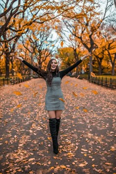 a woman standing in the middle of a leaf covered road with her arms outstretched up