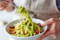 a person is holding a bowl of spaghetti with pesto and cherry tomatoes on top