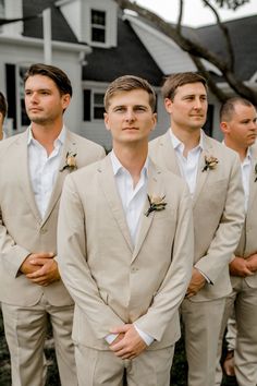 a group of men standing next to each other in front of a white house wearing tan suits