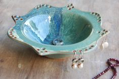 a blue bowl sitting on top of a wooden table next to a beaded necklace