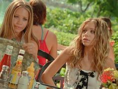 two young women sitting at an outdoor table with drinks and condiments in front of them