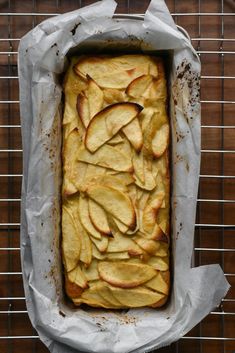 an apple cake in a baking pan on a cooling rack with parchment paper around it