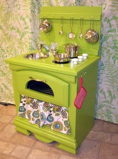 an old fashioned green stove with pots and pans on the oven door, in front of a floral wallpaper