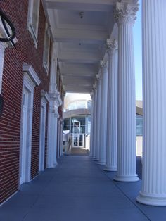 an empty sidewalk between two white pillars in front of a red brick building with columns on both sides