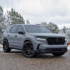 the front end of a gray suv parked on gravel with trees in the back ground