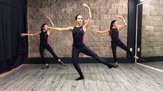 three women in black and pink outfits are dancing on a wooden floor with their arms stretched out