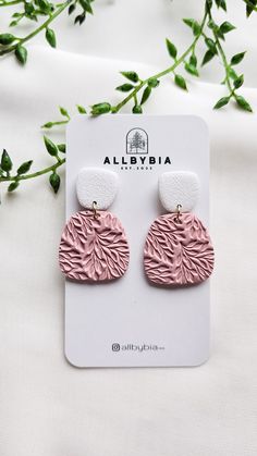 the pink and white earrings are on display next to some green leaves in front of a white