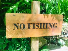 a wooden sign that says no fishing on it in front of some trees and bushes