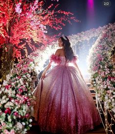 a woman in a pink dress is walking down the stairs with flowers on either side