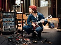 a man sitting on the floor with his guitar in front of him and recording equipment behind him