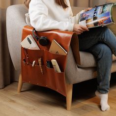 a woman sitting on a couch reading a magazine and holding a bag full of office supplies