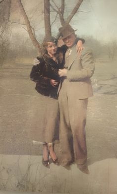 two people standing next to each other in front of trees and snow covered ground with one person hugging the other