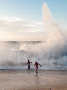 two people are running on the beach in front of an ocean spray