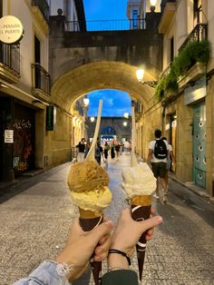 two ice cream cones are being held up in the air by someone's hand