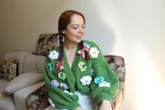 a woman sitting in a chair wearing a green sweater with flowers on it and smiling