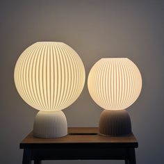 two lamps sitting on top of a wooden table next to each other in front of a gray wall