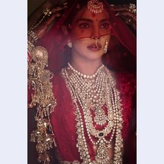 a woman in red and gold outfit with jewelry on her head, wearing an elaborate necklace