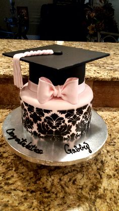 a decorated graduation cake with a pink bow on the top and black damask design