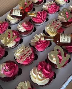 cupcakes decorated with pink and gold frosting are displayed in a cardboard box