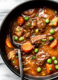 beef stew with carrots, peas and potatoes in a black bowl on a marble surface