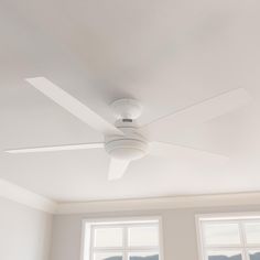 a white ceiling fan sitting in the middle of a living room next to two windows