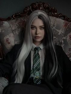 a woman with long white hair wearing a tie and sitting on a chair in a dark room