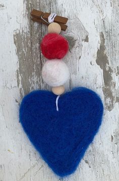 a blue felt heart hanging on a wooden wall with a red and white pom - pom attached to it