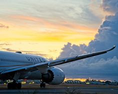 an airplane sitting on the tarmac at sunset with clouds in the sky behind it