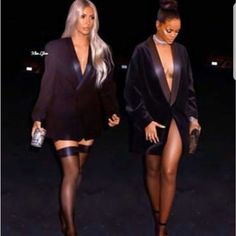 two women in black outfits walking down the street at night with one wearing thigh high stockings