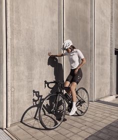 a man riding a bike next to a tall building with a shadow on the wall