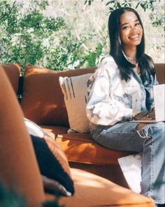 a woman sitting on top of a brown couch next to a forest filled with trees