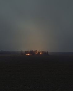 the sky is very dark and cloudy with some lights shining on trees in the distance