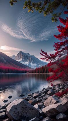 the mountains are covered in snow and red trees, along with rocks on the shore