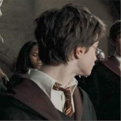 a young man with glasses and a tie standing in front of other people wearing harry potter robes